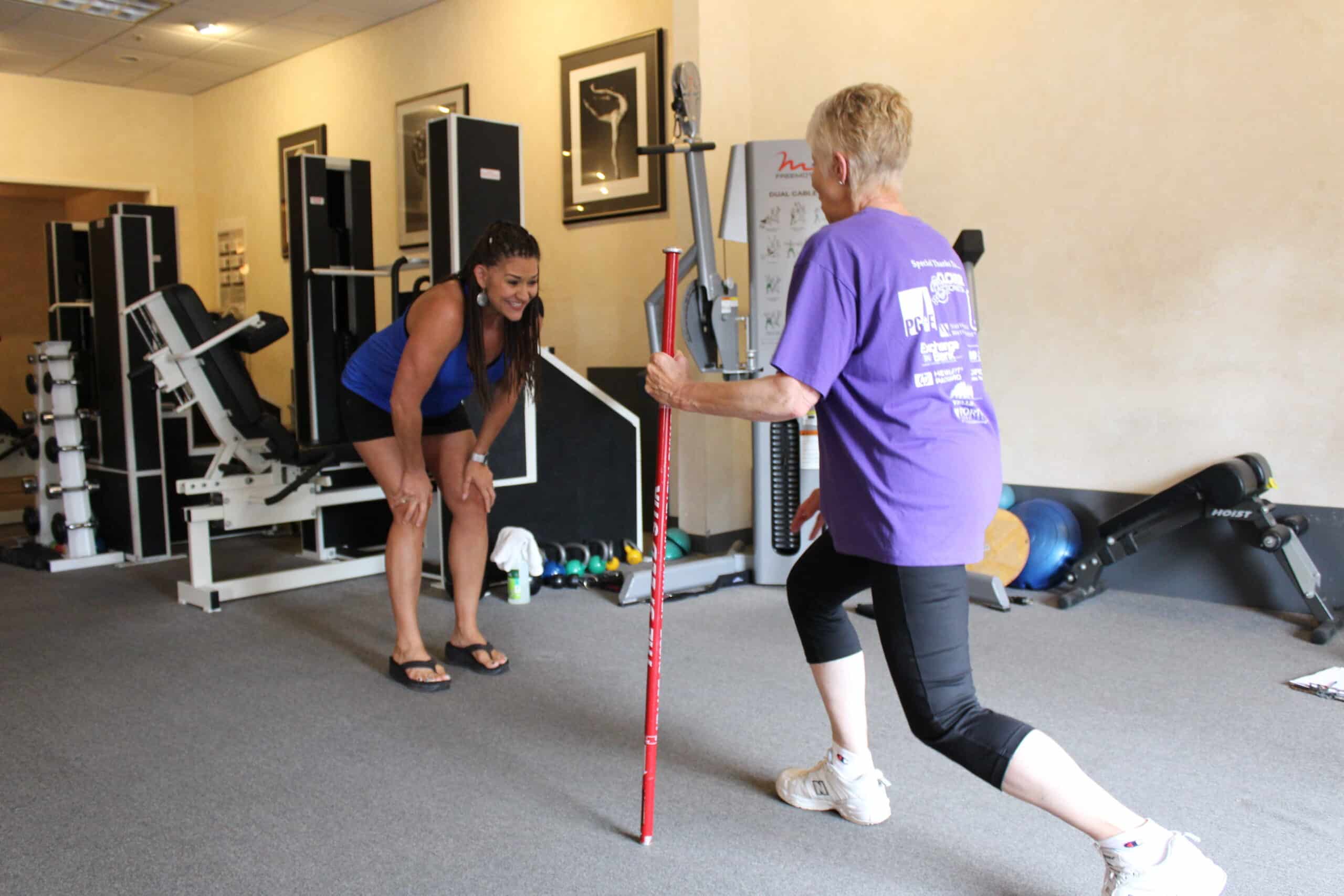 A woman in a purple shirt is holding a pole in a gym. This eye-catching image would be perfect for the homepage of a gym website, enhancing its SEO by attracting visitors with engaging visual content.