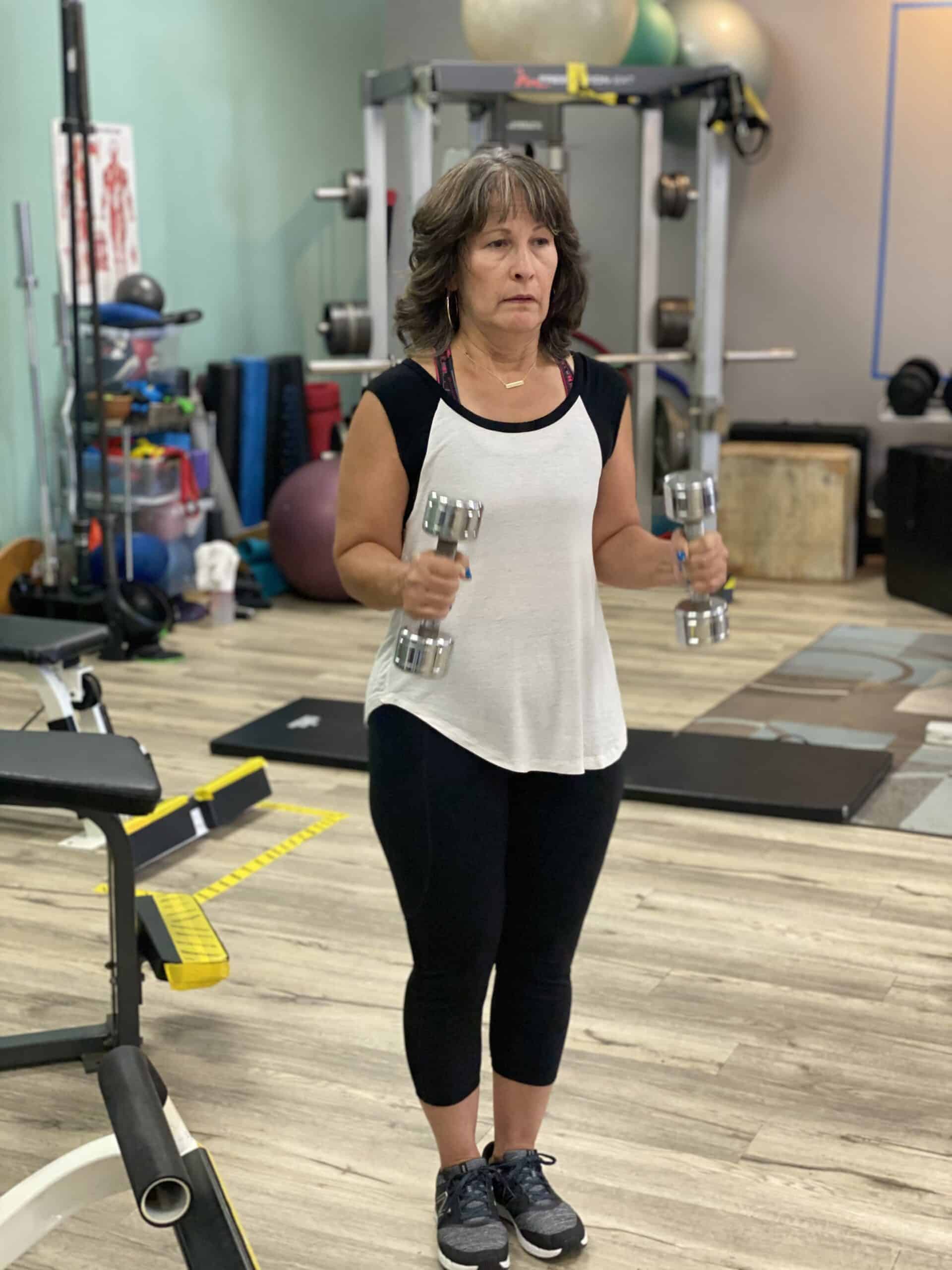 A woman standing in a gym holding dumbbells.