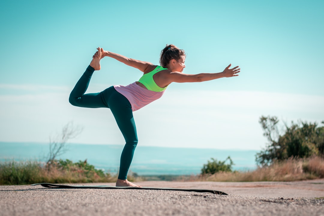Person practicing yoga outdoors, balancing on one leg in a dancer pose on a mat, with clear sky and distant landscape in the background—an inspiring scene of balance improvement and stability training. Person practicing yoga outdoors, balancing on one leg in a dancer pose on a mat, with clear sky and distant landscape in the background—an inspiring scene of balance improvement and stability training.