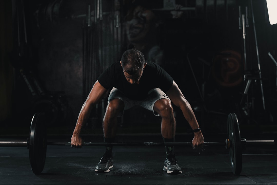 A person in athletic wear is preparing to lift a barbell in a dimly lit gym, using strength training as part of their natural prediabetes management routine. A person in athletic wear is preparing to lift a barbell in a dimly lit gym, using strength training as part of their natural prediabetes management routine.